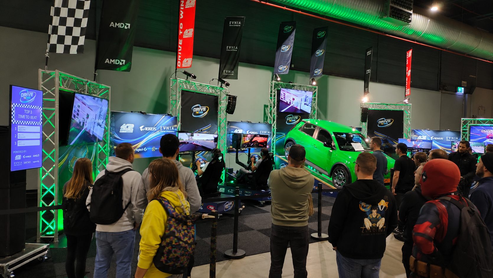 Bezoekers kijken toe terwijl deelnemers een ronde rijden op de Drive To Win-stand